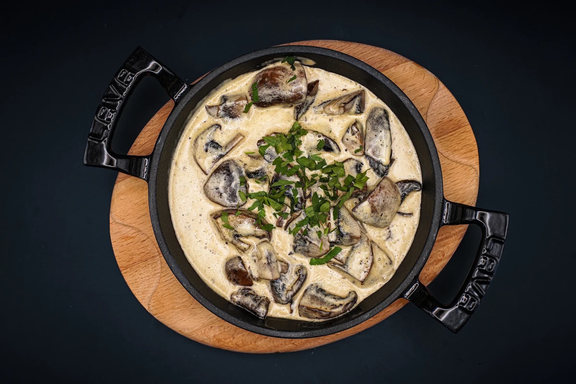 Creamy mushrooms in a cast-iron pan on a wooden board